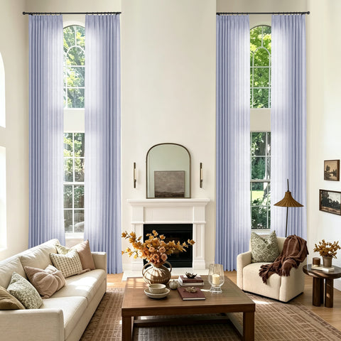 A styled living room with two tall arched windows dressed in light lavender blue sheer curtains