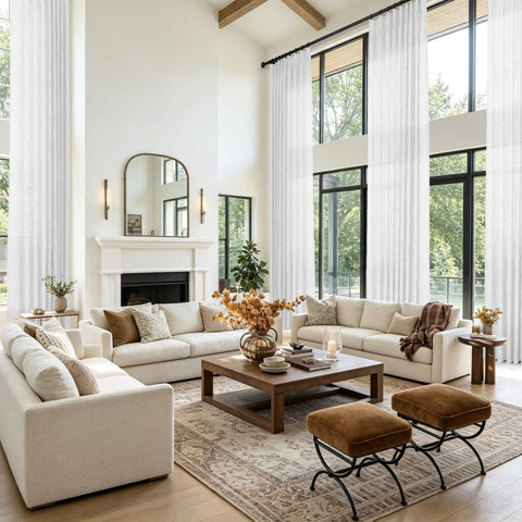 A bright modern living room featuring a cream sectional sofa set against a backdrop of tall windows and white sheer curtains and a white fireplace