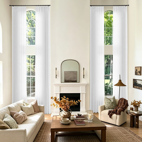 A pair of long white pleated window curtains hanging on black metal rods in a bright modern living room