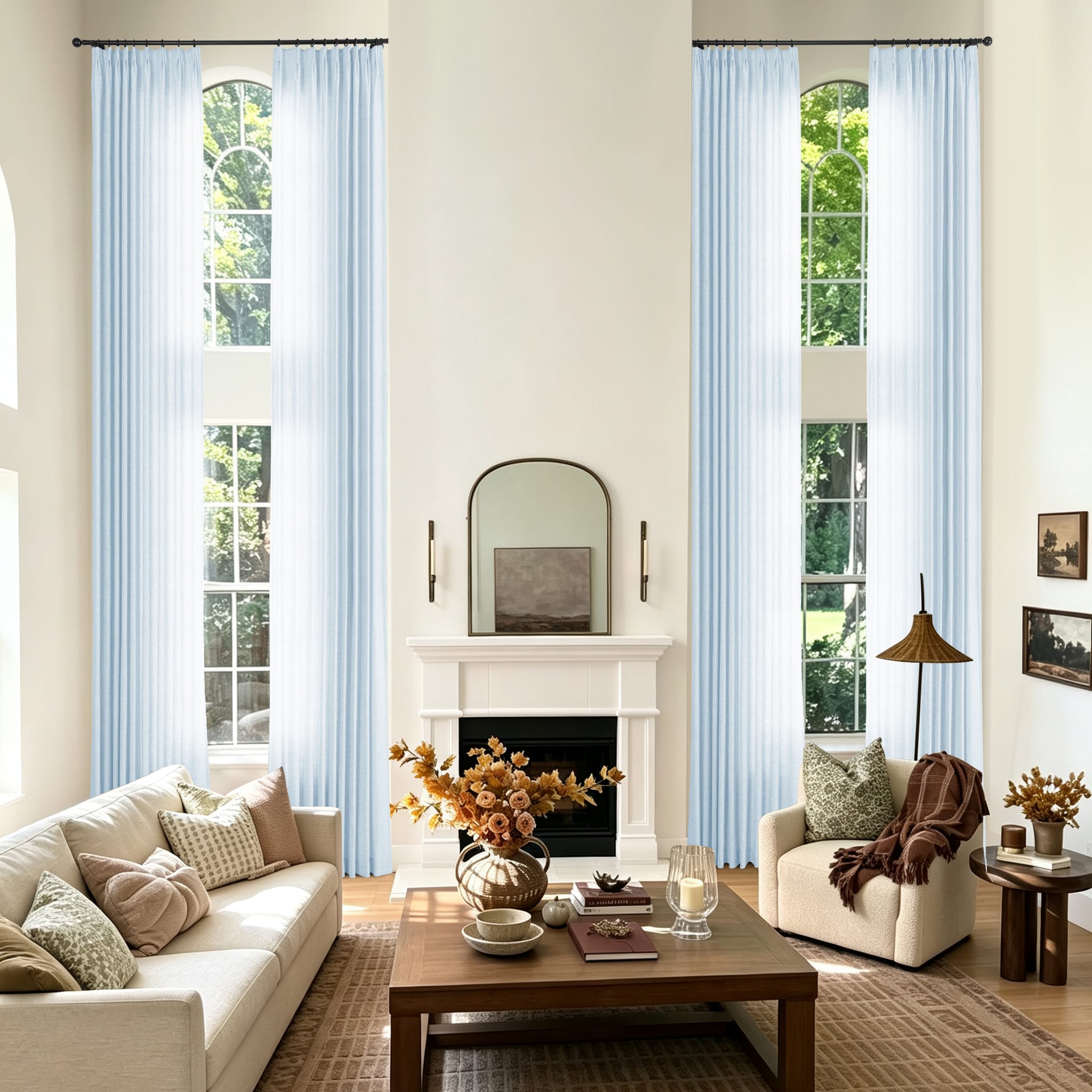 A styled living room with two tall windows dressed in light blue sheer curtains featuring a cream sofa and a chair with a throw blanket