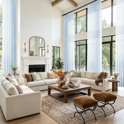 A bright modern living room with a large cream sectional sofa and light blue sheer curtains hanging in tall windows